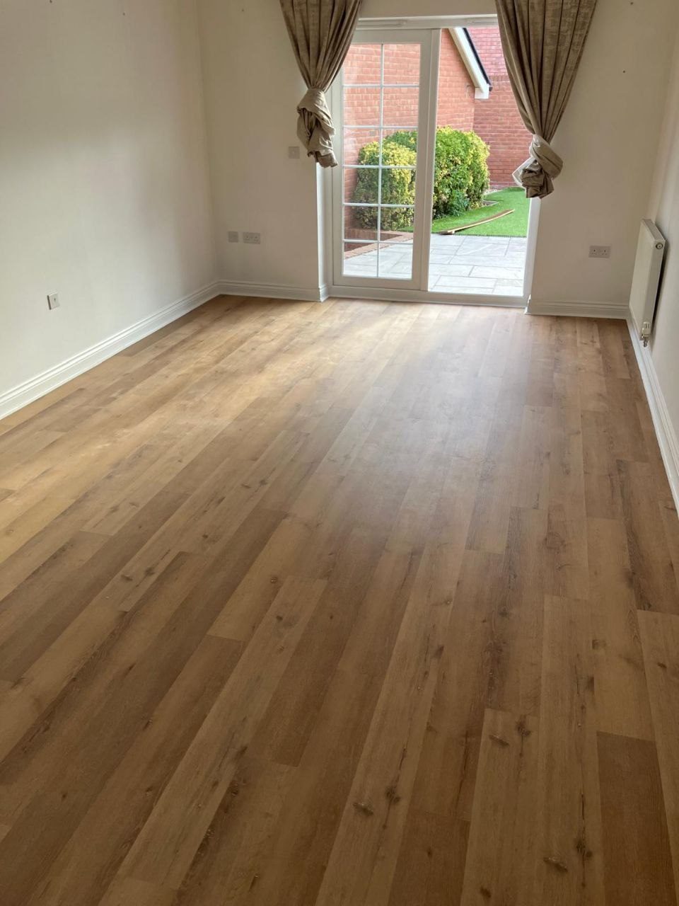 Mid oak LVT flooring laid across a room and up to a set of French doors opening onto a garden