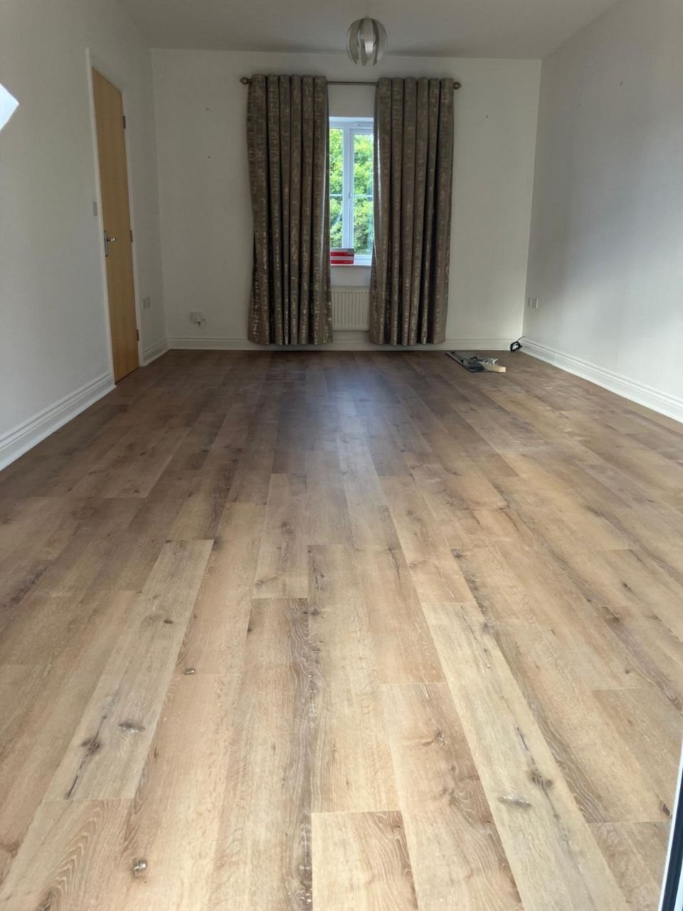 Light oak LVT flooring laid across an empty room, finished with a scotia bead at the edge