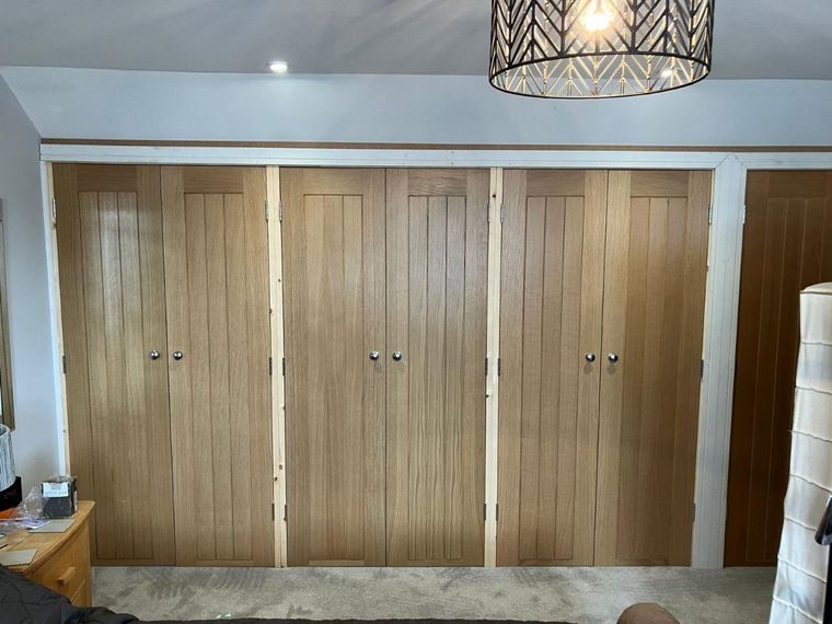 Wall of fitted wardrobes with oak cottage style doors