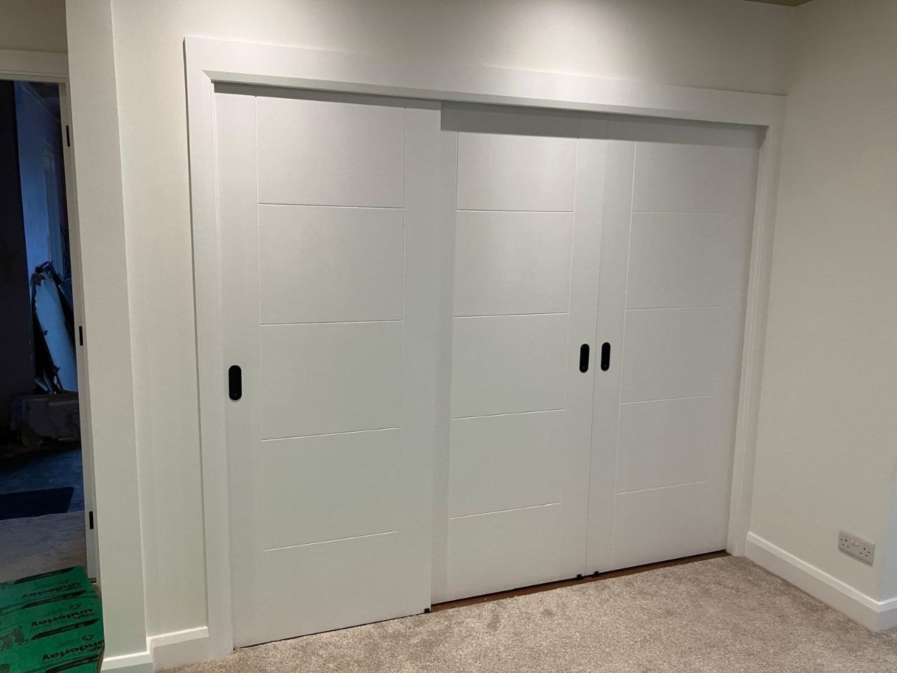 Three white shaker sliding wardrobe doors fitted across a bedroom recess