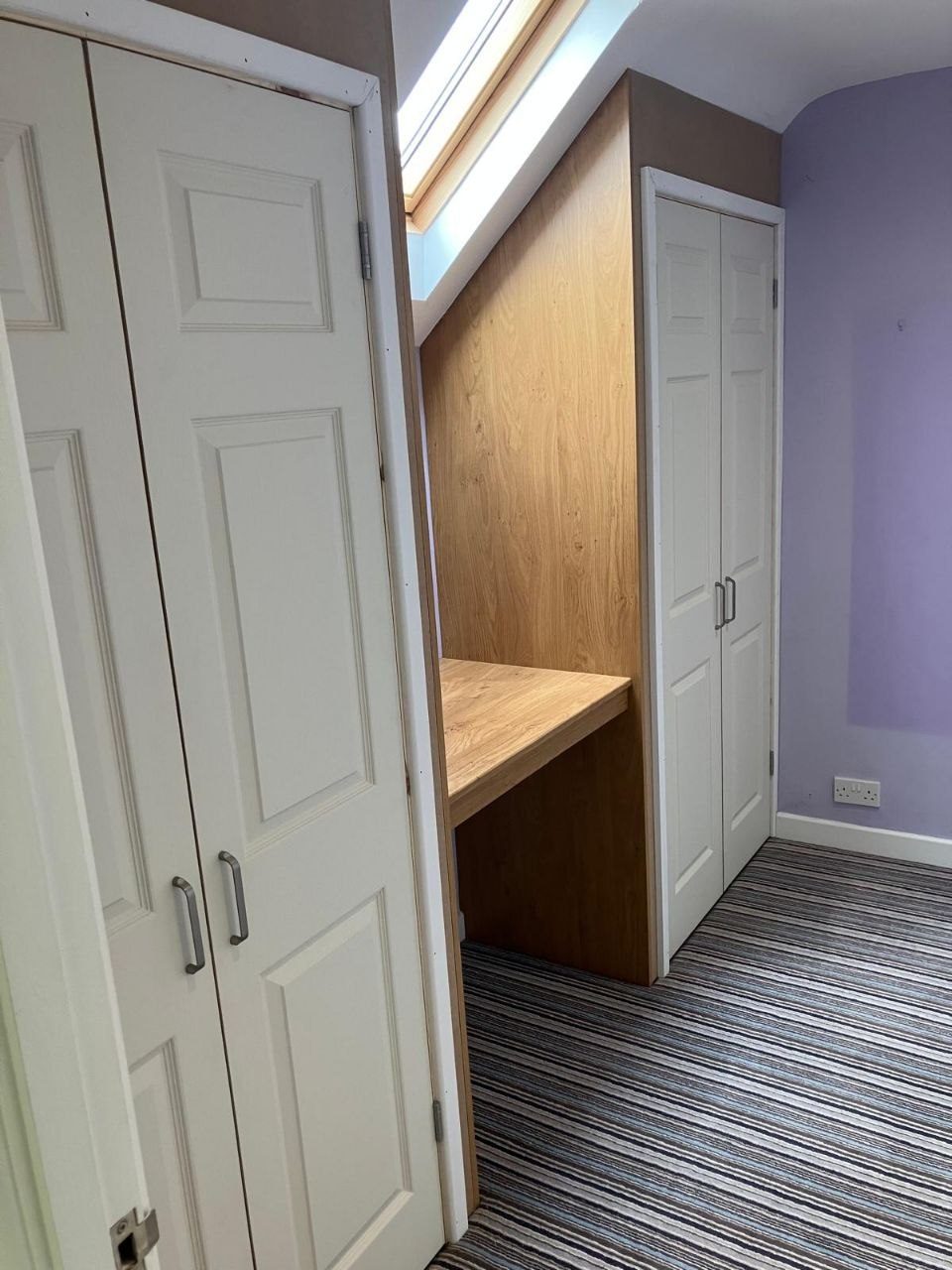 Oak lined desk built into the eaves beneath a roof window, with fitted wardrobes either side