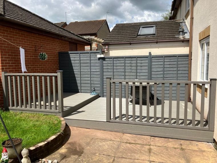 Raised composite deck with matching handrail and spindles across a back garden