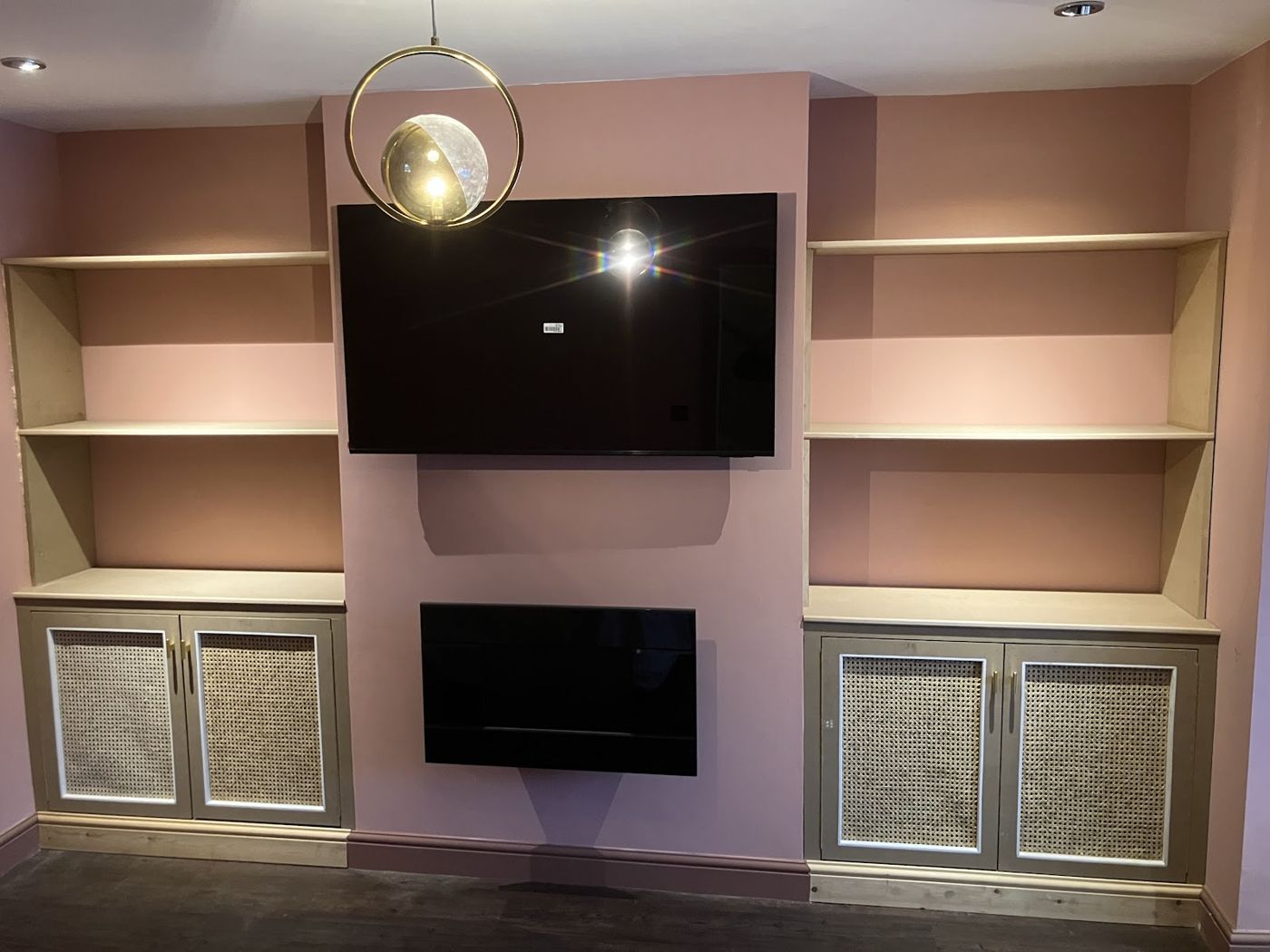 Media wall with rattan fronted cupboards, brass handles and open shelving either side of a wall mounted television and fire
